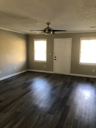 an empty room with wooden floor chandelier fan and windows