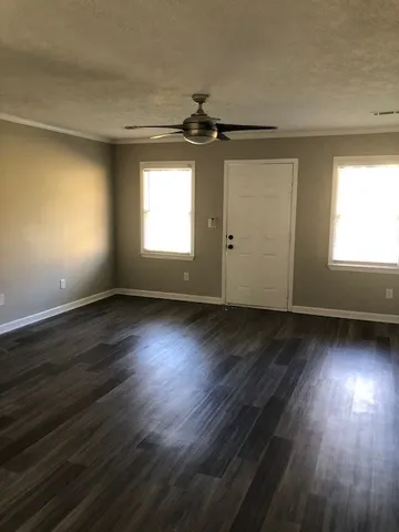 an empty room with wooden floor chandelier fan and windows