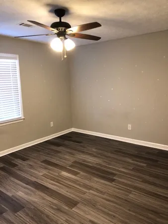 a view of an empty room with wooden floor and a fan