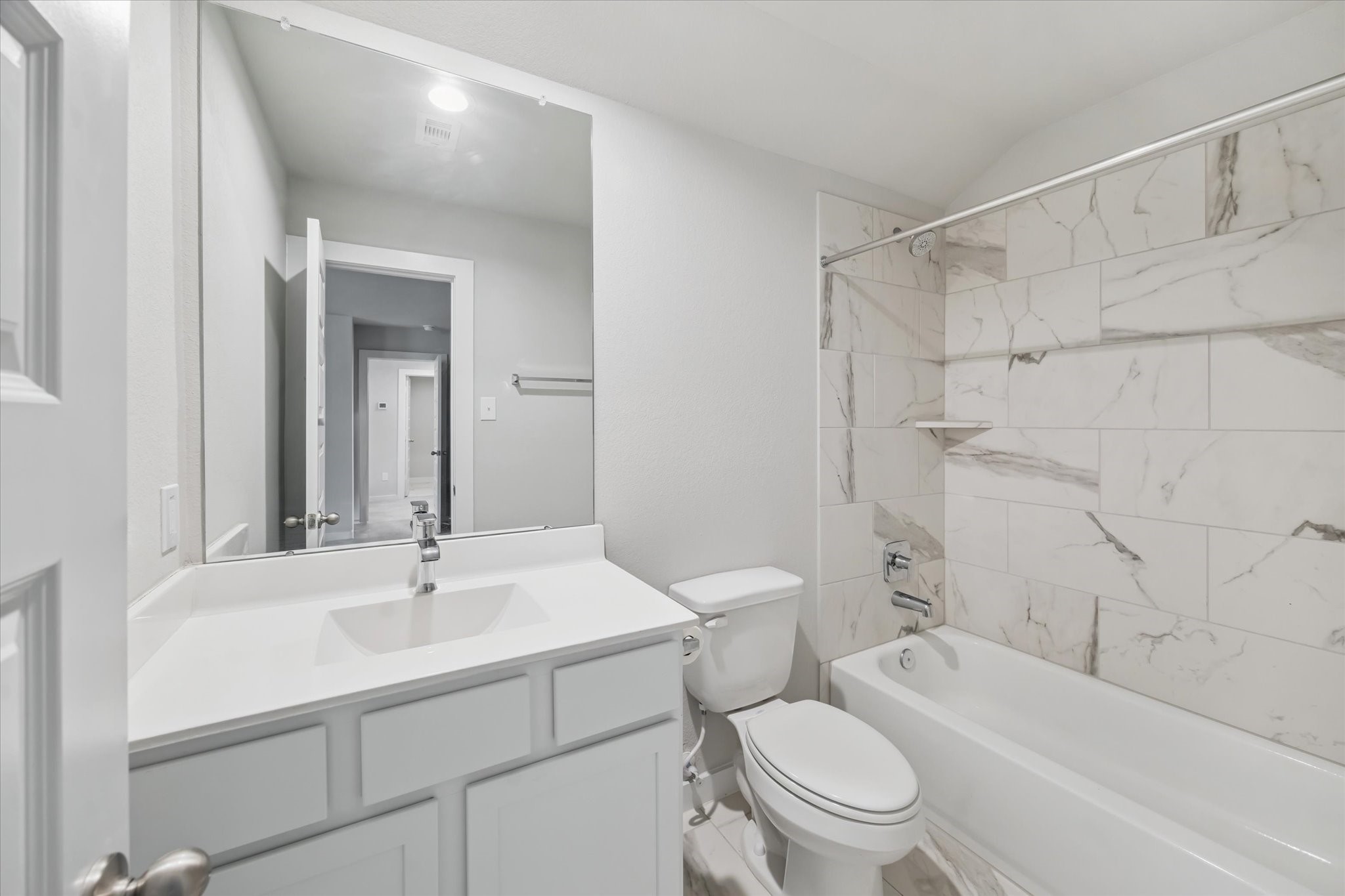 2138 Reed Cave Lane Spring, TX 77386 - Photo 14 of 23 This en-suite bathroom features a modern design with a white vanity, polished countertop, and a large mirror. The bathtub is complemented by elegant marble-style tile, creating a bright and clean atmosphere.