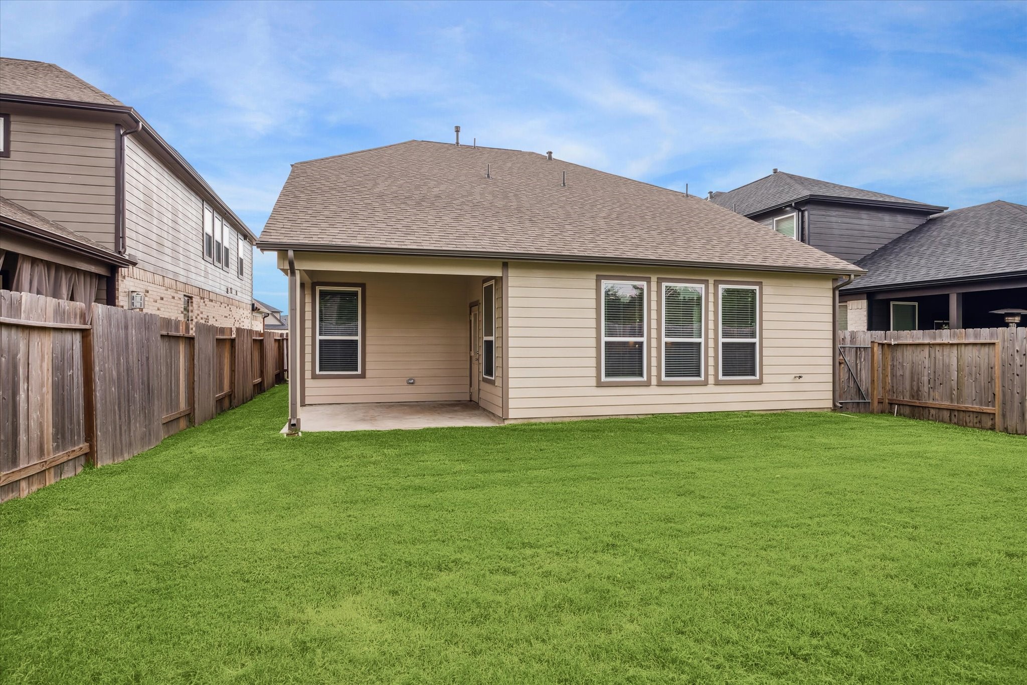 2138 Reed Cave Lane Spring, TX 77386 - Photo 20 of 23 This photo shows a backyard with a well-maintained lawn and a covered patio area, ideal for outdoor activities and relaxation. The house features a modern exterior with multiple windows, ensuring plenty of natural light. A wooden fence encloses the yard, providing privacy.