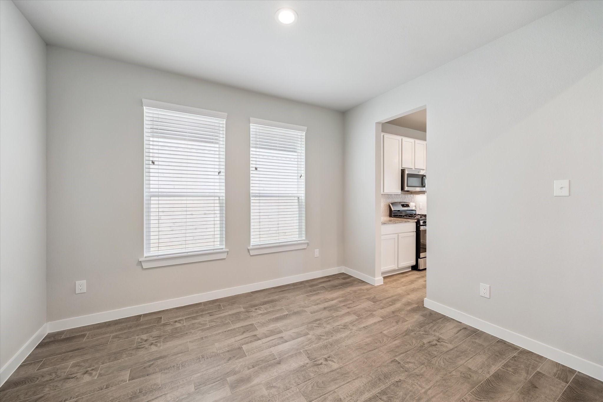 2138 Reed Cave Lane Spring, TX 77386 - Photo 7 of 23 This room features light wood flooring, neutral walls, and two large windows providing natural light. It opens into a kitchen with modern appliances and white cabinetry. Ideal for a dining space.