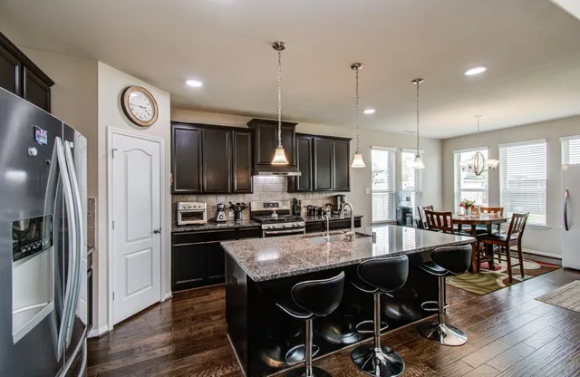 a kitchen with stainless steel appliances granite countertop a stove a refrigerator a kitchen island a dining table and chairs with wooden floor