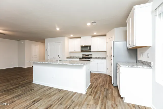 a kitchen with stainless steel appliances granite countertop a sink a stove a refrigerator and white cabinets with wooden floor