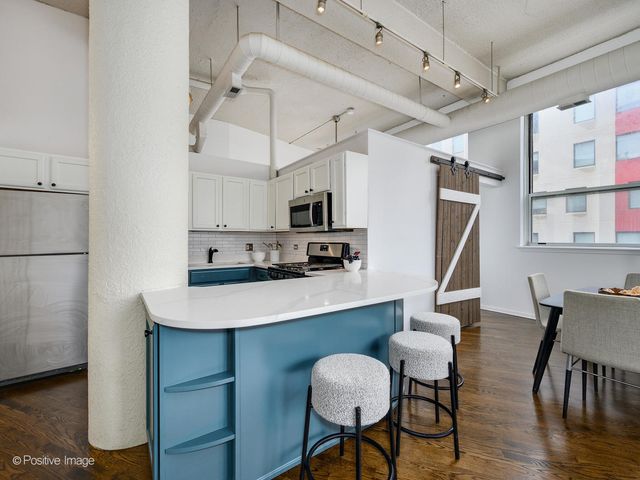 a kitchen with stainless steel appliances granite countertop a dining table chairs refrigerator and microwave