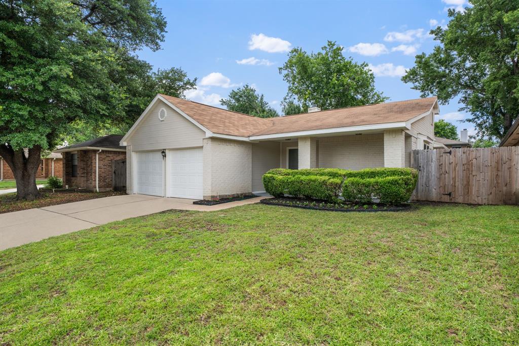 310 Valley Spring Drive Arlington, TX 76018 - Photo 2 of 24 Front exterior featuring light-colored brick siding, a two-car garage, a covered entry, a neatly trimmed shrub bed, and a wood privacy fence