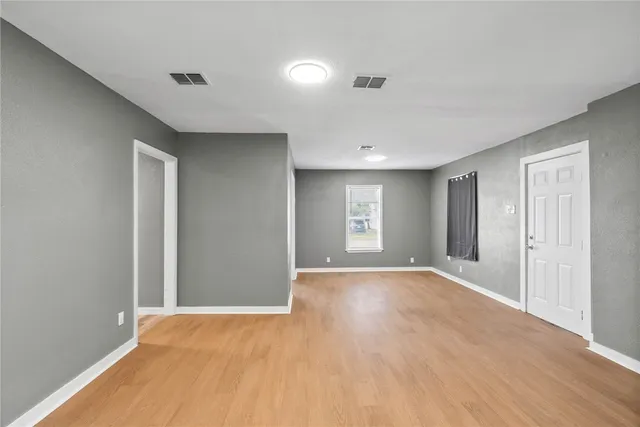 a view of an empty room with window and wooden floor