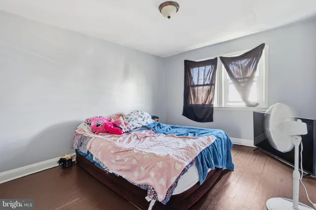 a bedroom with a bed and dresser with wooden floor