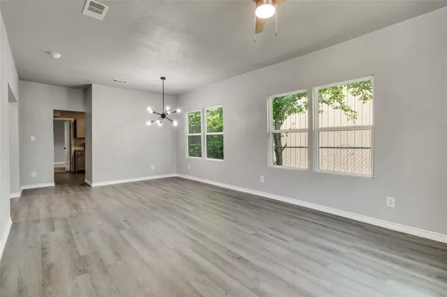an empty room with wooden floor chandelier and windows