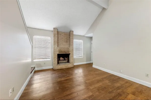 a view of an empty room with wooden floor fireplace and a window