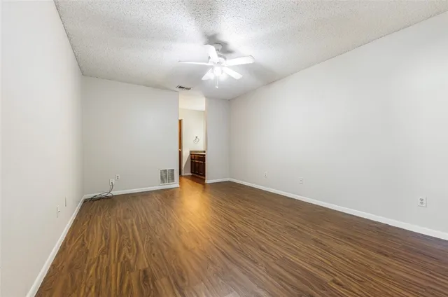 a view of an empty room with wooden floor and a ceiling fan