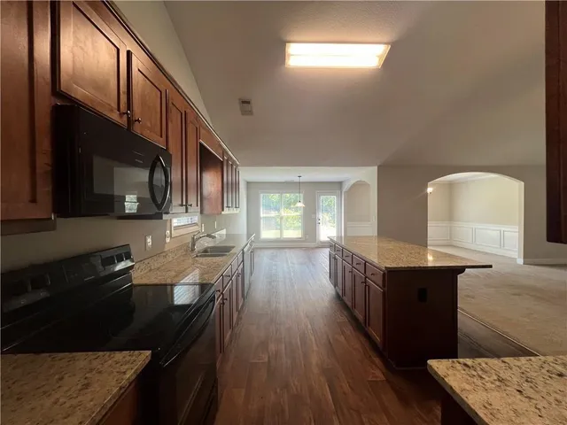 a kitchen with granite countertop a stove a sink dishwasher and cabinets with wooden floor