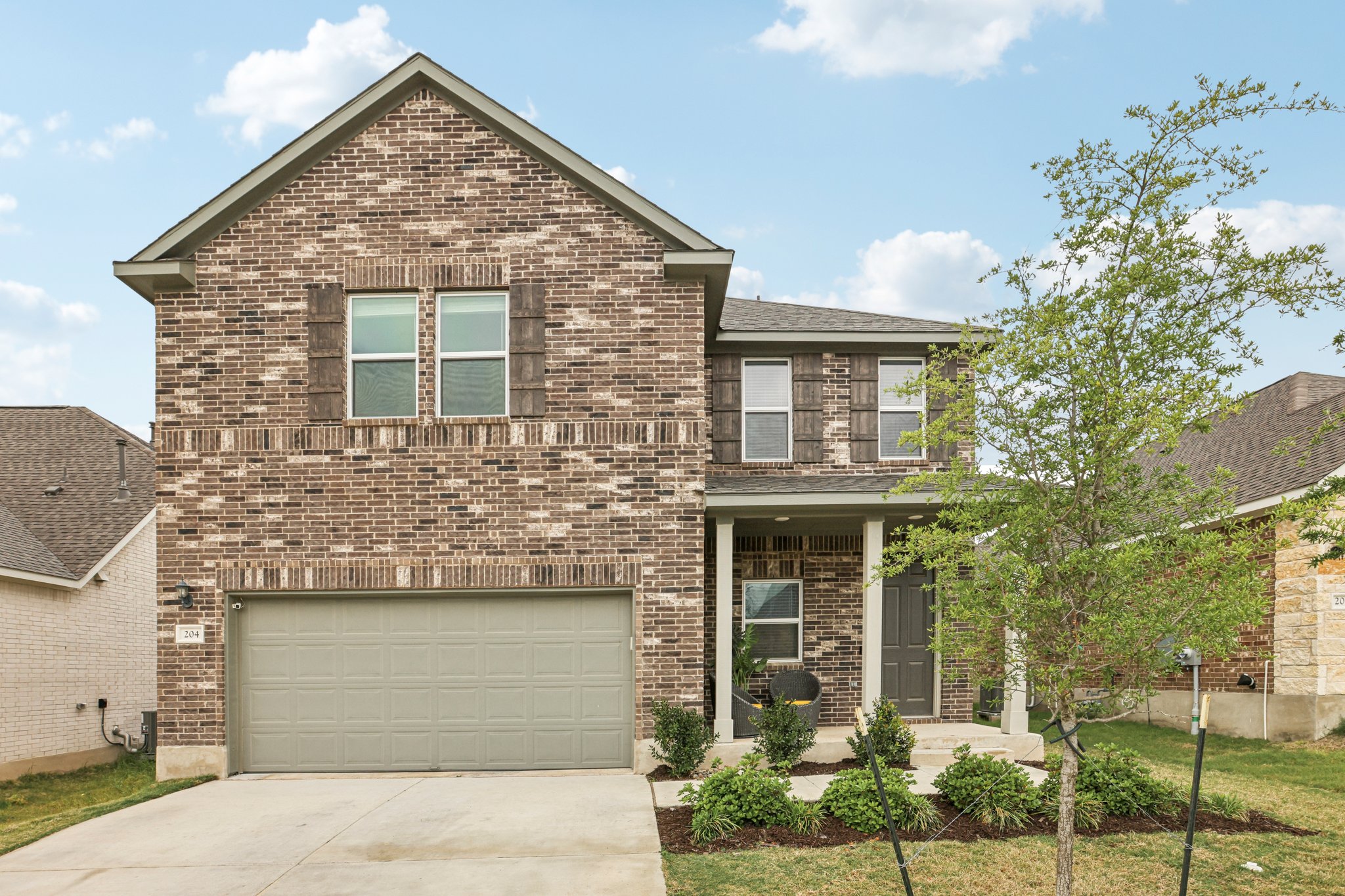 204 Swinging H Lane Georgetown, TX 78633 - Photo 2 of 39 The property features a brick exterior, an attached garage, a covered front porch, and a well-maintained front yard with landscaping