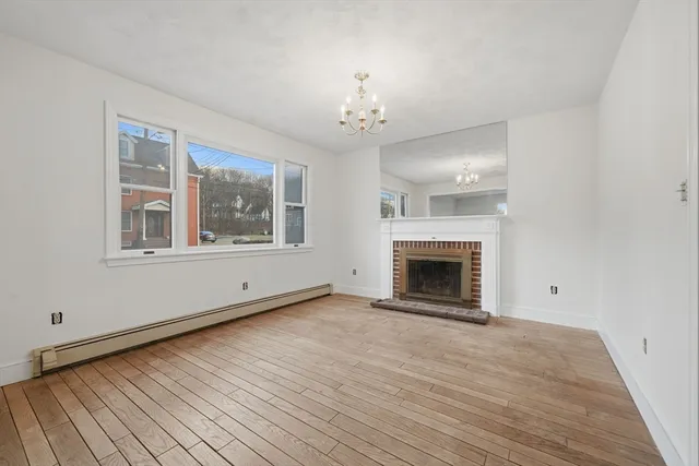 a view of an empty room with wooden floor fireplace and a window