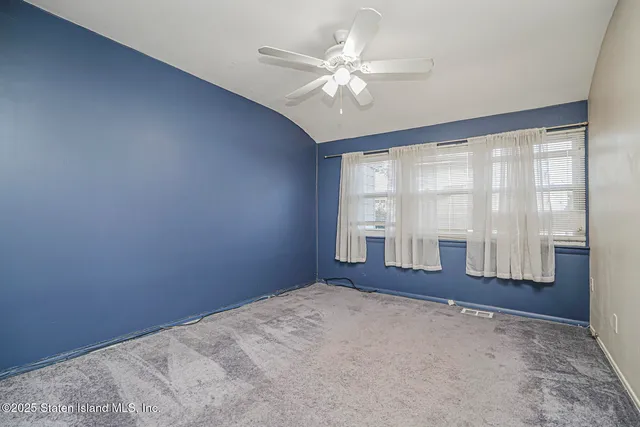 an empty room with chandelier fan and windows