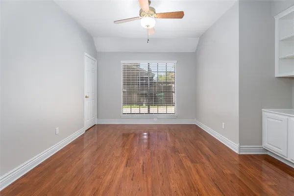 an empty room with wooden floor chandelier fan and windows