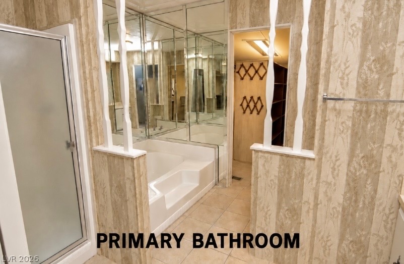 4556 Royal Ridge Way Las Vegas, NV 89103 - Photo 16 of 49 Textured walls and tiled flooring frame a built-in soaking tub beneath mirrored panels.