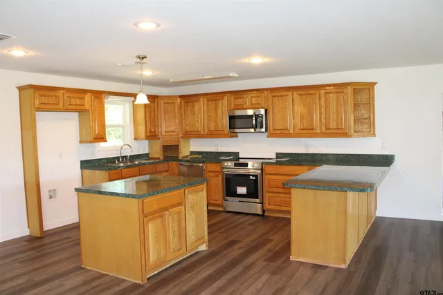 a kitchen with stainless steel appliances granite countertop wooden cabinets a sink a stove a refrigerator and island with wooden floor