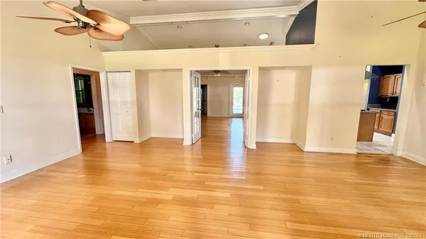 a view of an empty room with wooden floor and a ceiling fan