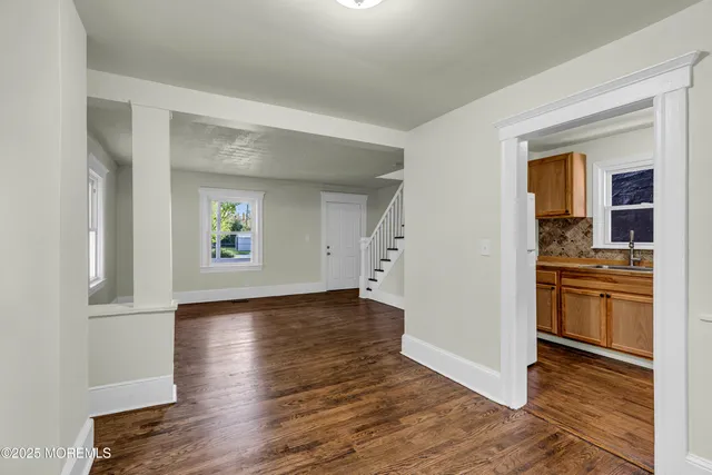 an empty room with wooden floor and a kitchen
