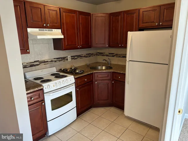 a white refrigerator freezer and a stove sitting inside of a kitchen with granite countertop wooden cabinets