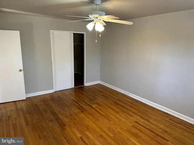 a view of an empty room with chandelier fan and wooden floor