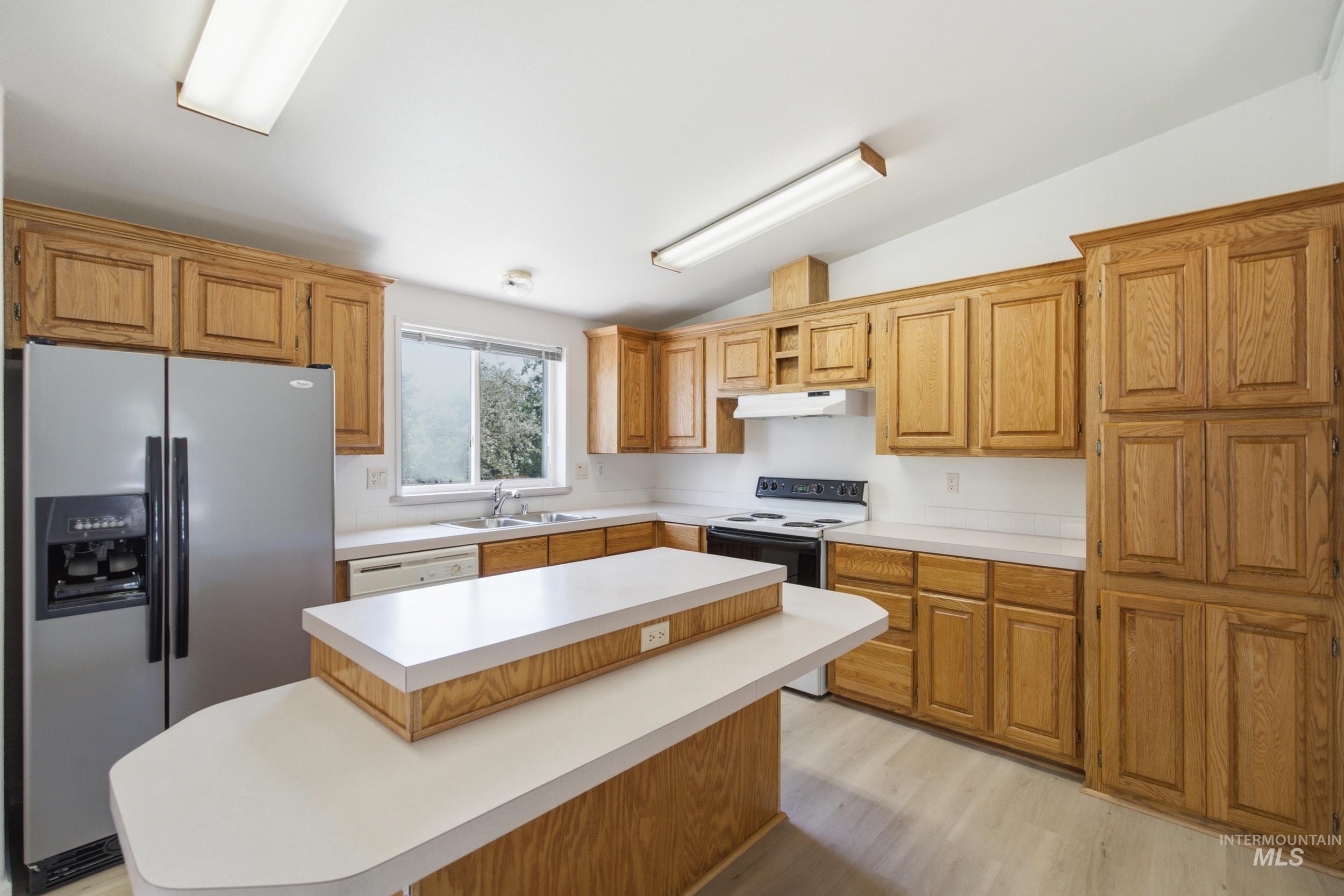 7422 Track Road Nampa, ID 83686 - Photo 6 of 50 Kitchen featuring extensive wood cabinetry, white countertops, a central island with a breakfast bar, stainless steel refrigerator, and a window above the sink