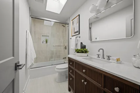a bathroom with a granite countertop sink a toilet a mirror and shower