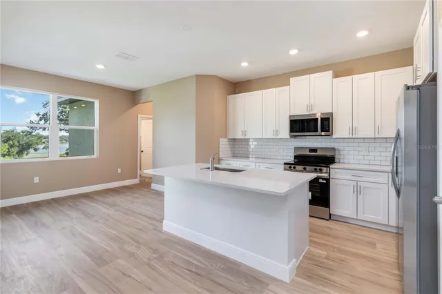 a kitchen with stainless steel appliances a microwave a stove a sink dishwasher a refrigerator and white cabinets with wooden floor