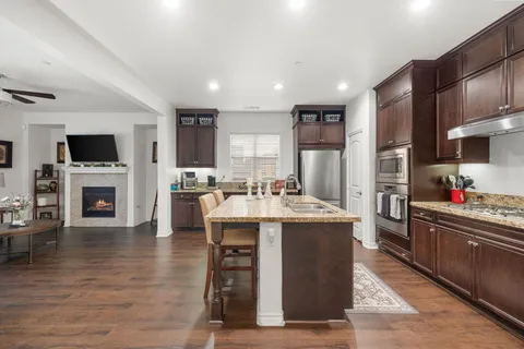 a kitchen with stainless steel appliances granite countertop a stove top oven a sink dishwasher a dining table and chairs with wooden floor
