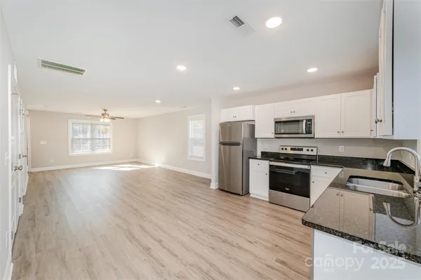 a kitchen with stainless steel appliances granite countertop a refrigerator a sink dishwasher a stove with wooden floors and cabinets
