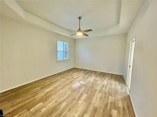 an empty room with wooden floor ceiling fan and windows