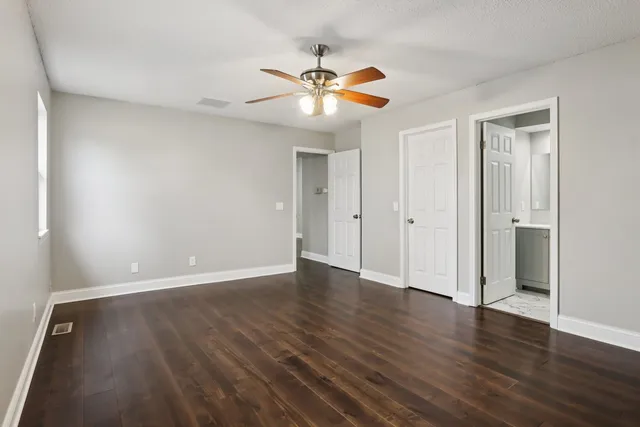 a view of an empty room with wooden floor and a ceiling fan