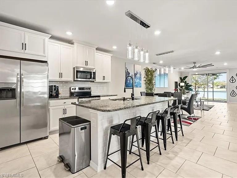 14672 Edgewater Circle Naples, FL 34114 - Photo 10 of 41 a kitchen with stainless steel appliances kitchen island granite countertop a sink a stove a refrigerator and a dining table with wooden floor