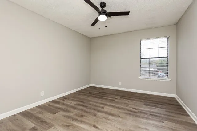 an empty room with wooden floor ceiling fan and windows