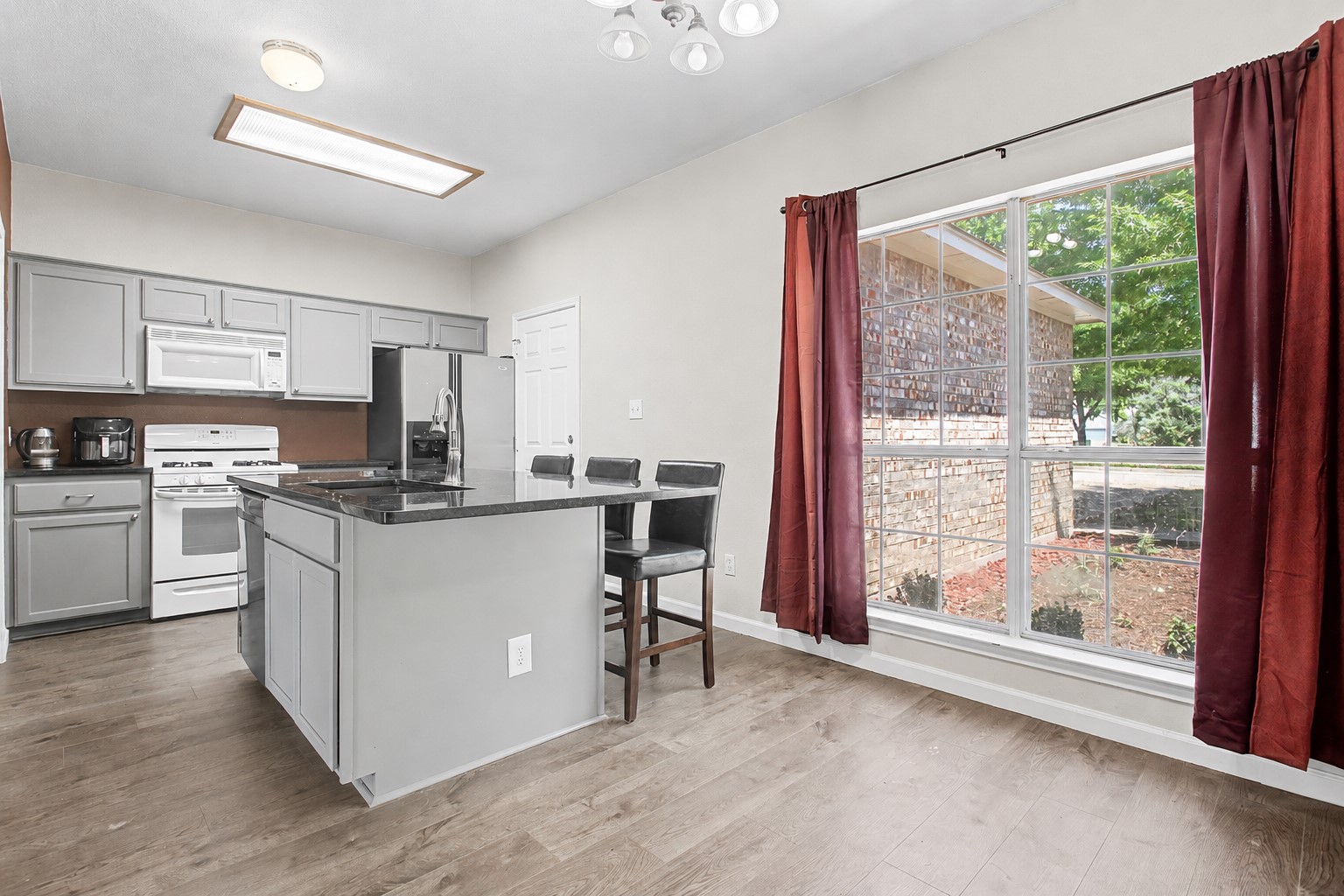207 Kates Way Hutto, TX 78634 - Photo 16 of 24 Kitchen featuring a central island with countertop seating, gray cabinetry, stainless steel refrigerator, white range, and a large picture window.
Photo digitally edited to remove personal items.