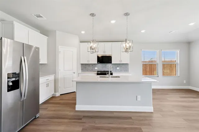 a kitchen with stainless steel appliances kitchen island granite countertop a refrigerator a stove a sink dishwasher a refrigerator and white cabinets with wooden floor