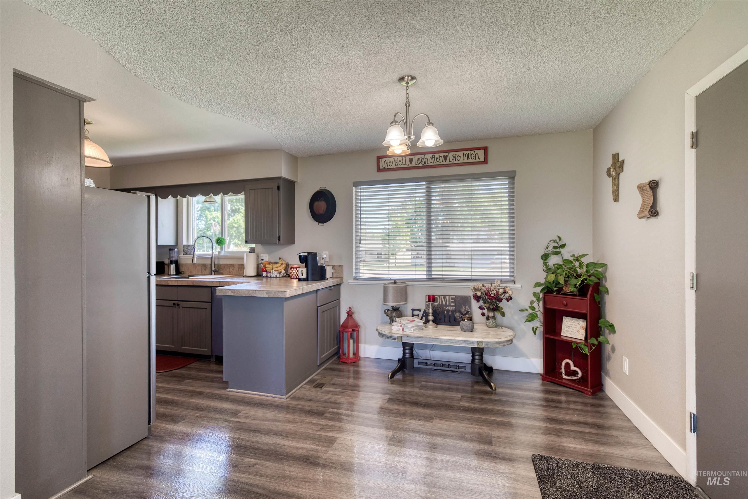 20803 Friends Road Greenleaf, ID 83626 - Photo 38 of 39 Kitchen and dining area featuring wood-finish flooring, gray cabinetry, stainless steel refrigerator, and ample natural light from a large window with blinds