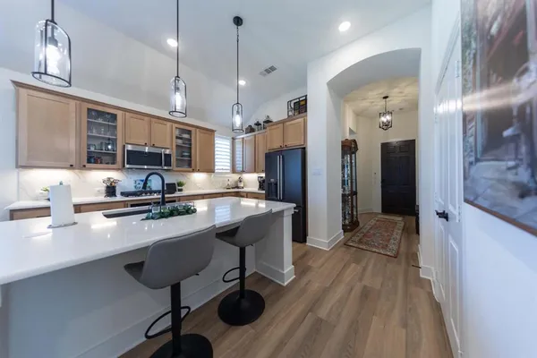 a room with stainless steel appliances kitchen island granite countertop furniture a refrigerator a sink and wooden floors