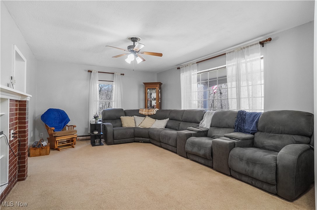 35977 Teegarden Road Salem, OH 44460 - Photo 17 of 50 Carpeted living area featuring baseboard heating, a textured ceiling, a ceiling fan, and a brick fireplace