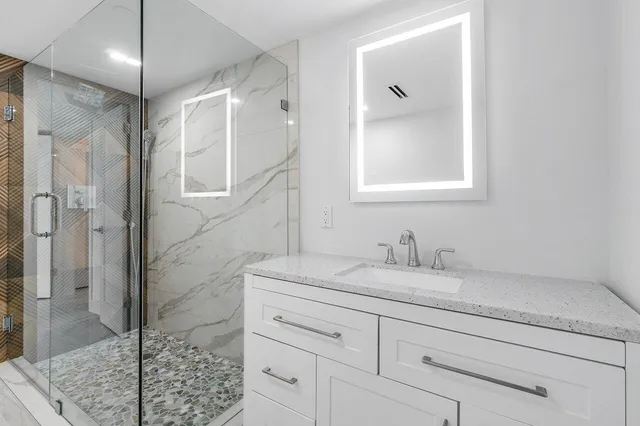 a bathroom with a granite countertop sink a mirror and shower