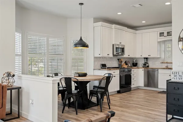 a kitchen with stainless steel appliances granite countertop a stove a sink a microwave a refrigerator and white cabinets with wooden floors