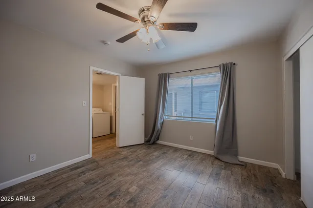 an empty room with wooden floor chandelier fan and windows