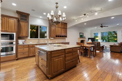 a kitchen with stainless steel appliances granite countertop wooden cabinets a sink dishwasher a stove and a dining table with wooden floor