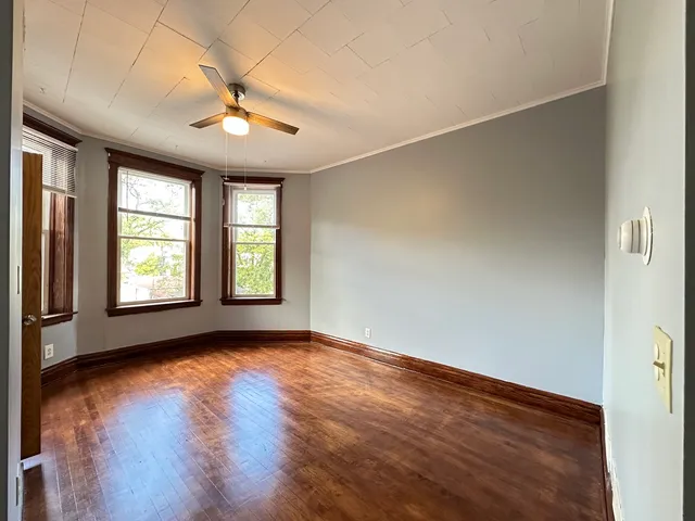 an empty room with wooden floor chandelier fan and windows