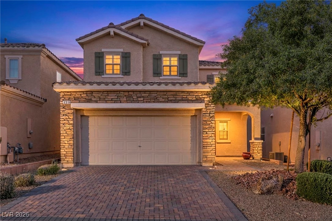 Mediterranean / spanish home featuring stone siding, decorative driveway, stucco siding, and an attached garage
