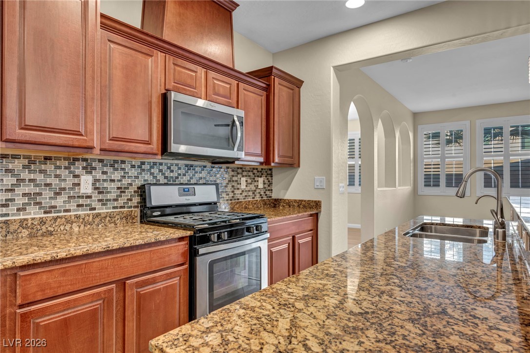 356 Aqua Springs Road Las Vegas, NV 89148 - Photo 11 of 39 Kitchen with appliances with stainless steel finishes, dark stone counters, arched walkways, and brown cabinetry