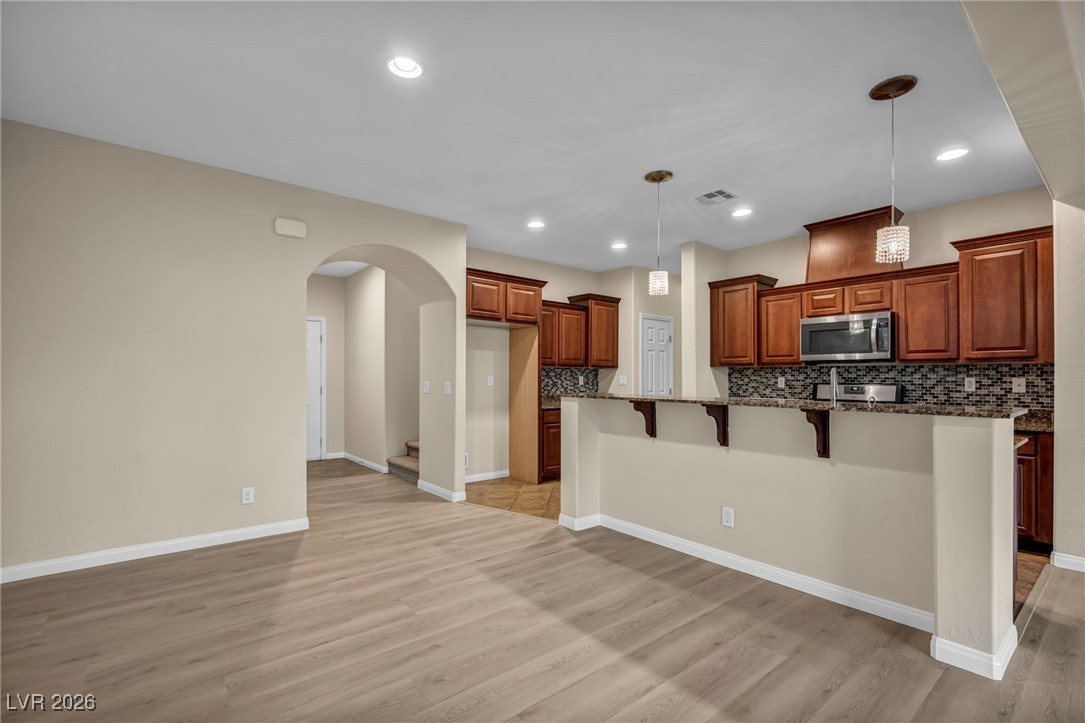 356 Aqua Springs Road Las Vegas, NV 89148 - Photo 12 of 39 Kitchen with a breakfast bar area, backsplash, arched walkways, pendant lighting, and stainless steel microwave