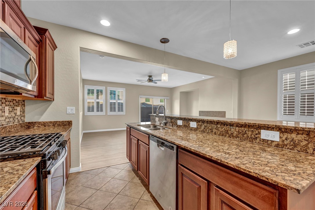 356 Aqua Springs Road Las Vegas, NV 89148 - Photo 13 of 39 Kitchen featuring light stone counters, hanging light fixtures, appliances with stainless steel finishes, brown cabinetry, and recessed lighting