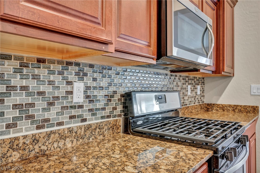 356 Aqua Springs Road Las Vegas, NV 89148 - Photo 14 of 39 Kitchen with appliances with stainless steel finishes, light stone counters, decorative backsplash, and brown cabinetry